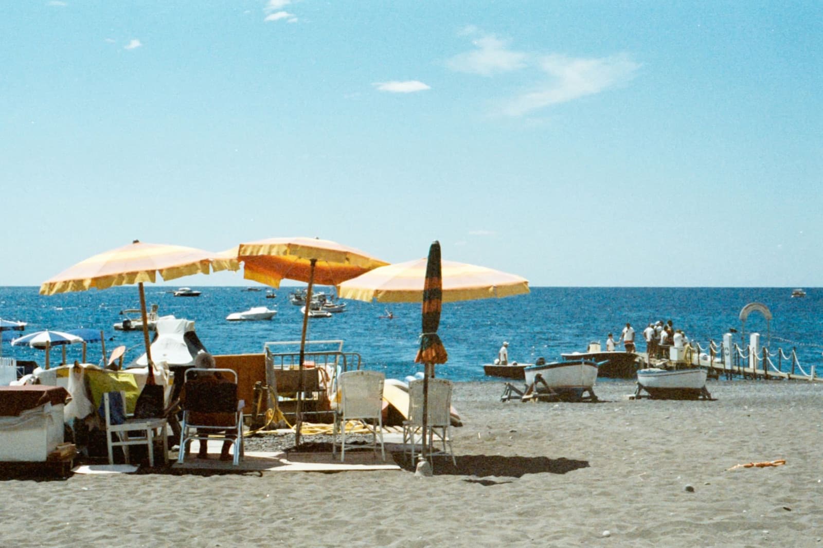 Beach with yellow umbrellas and small boats beneath a blue sky